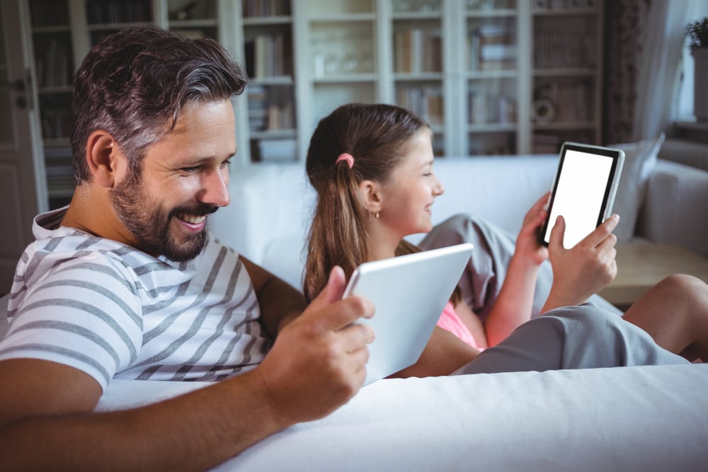 Father and daughter using digital tablet in living room at home